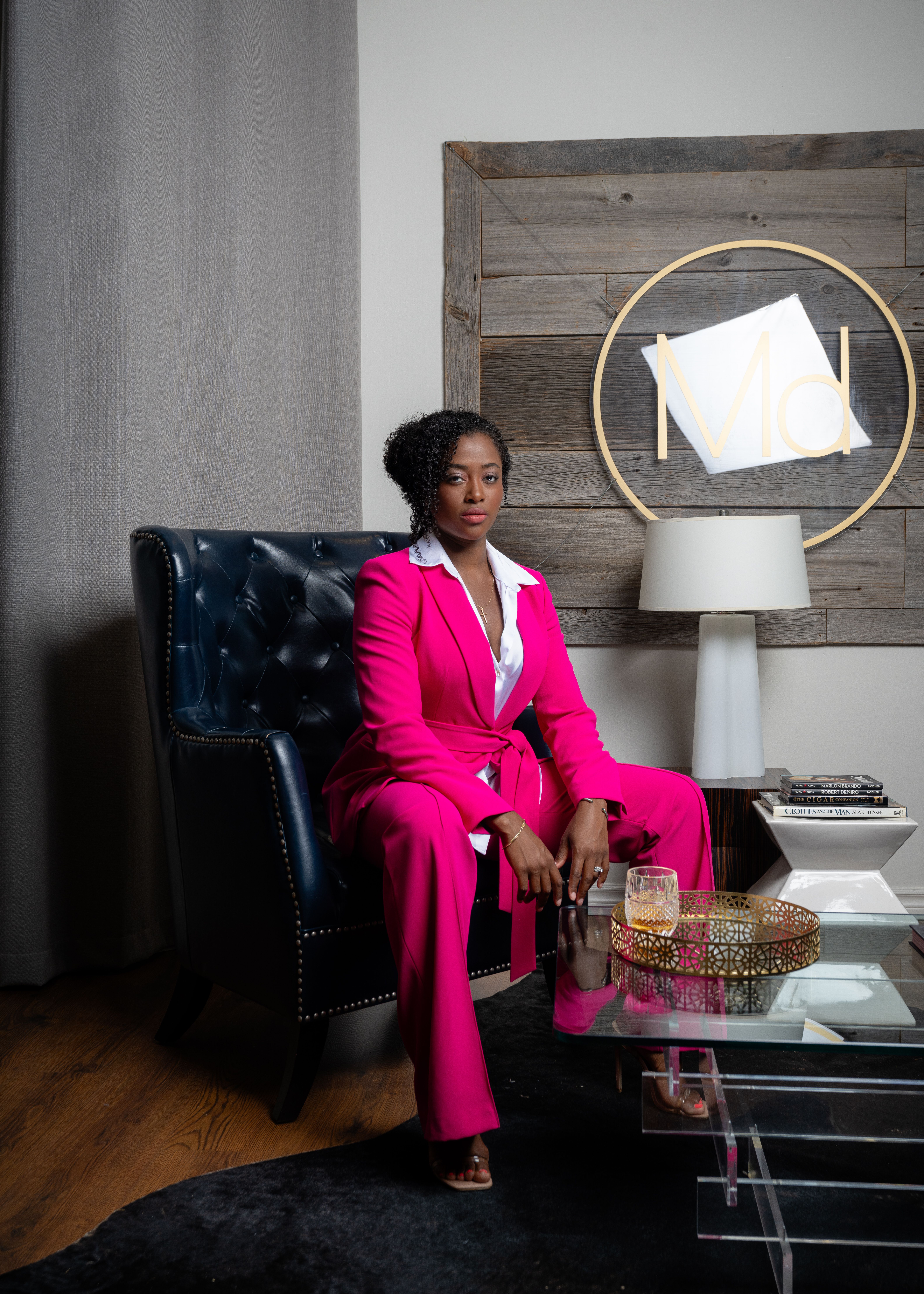 Portrait of a woman in a bold pink suit seated in a stylish living room setting.