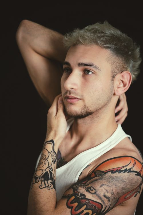 Free Close-up portrait of a young man with tattoos and blonde hair against a black background. Stock Photo