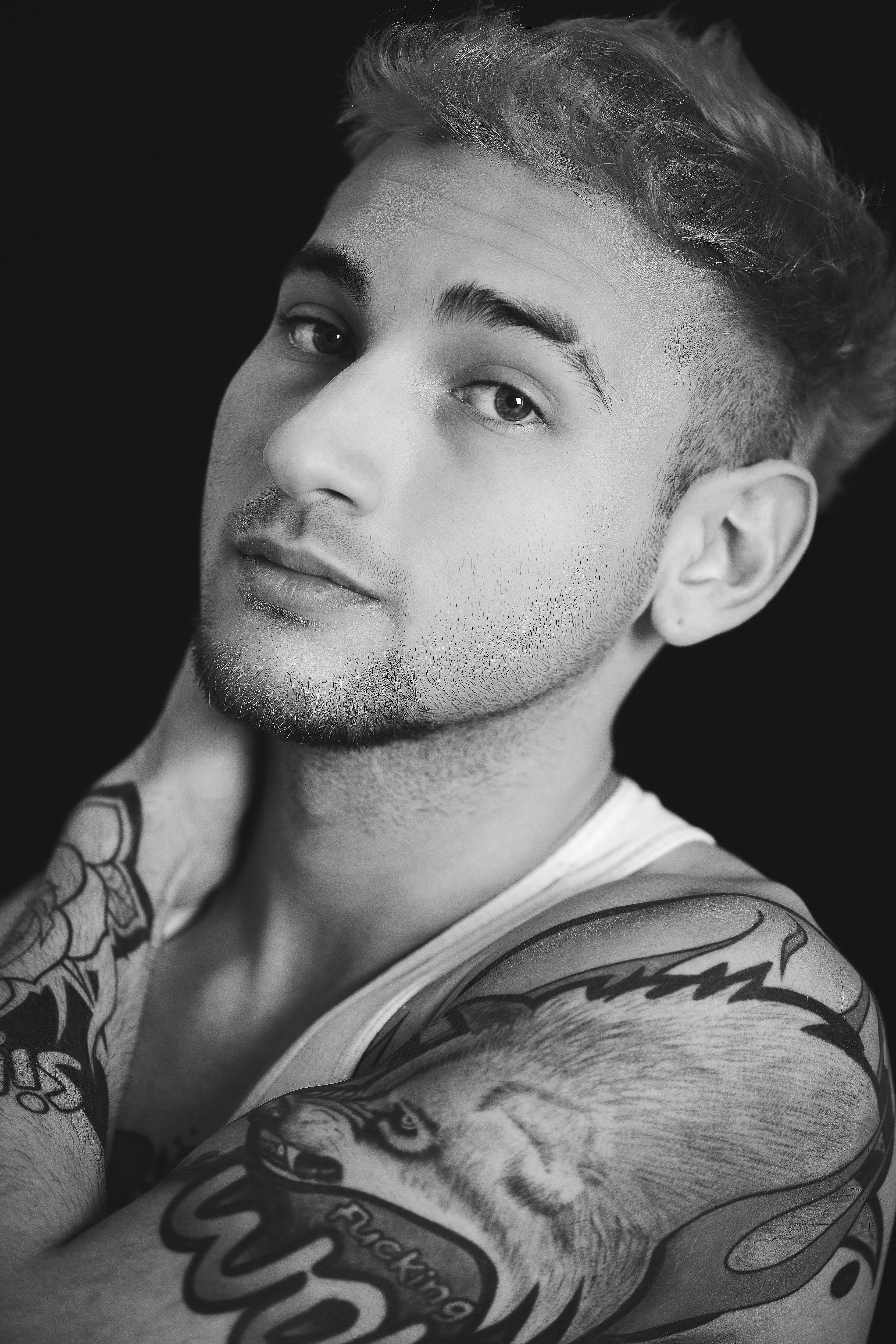 Black and white close-up of a tattooed young man staring thoughtfully.