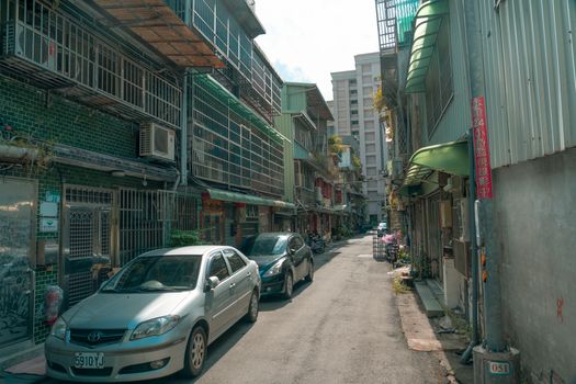 A narrow urban alley lined with residential buildings and parked cars on a sunny day.