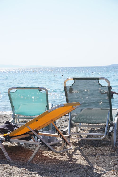 Free Idyllic beach view in Greece with deckchairs by the shimmering sea. Stock Photo