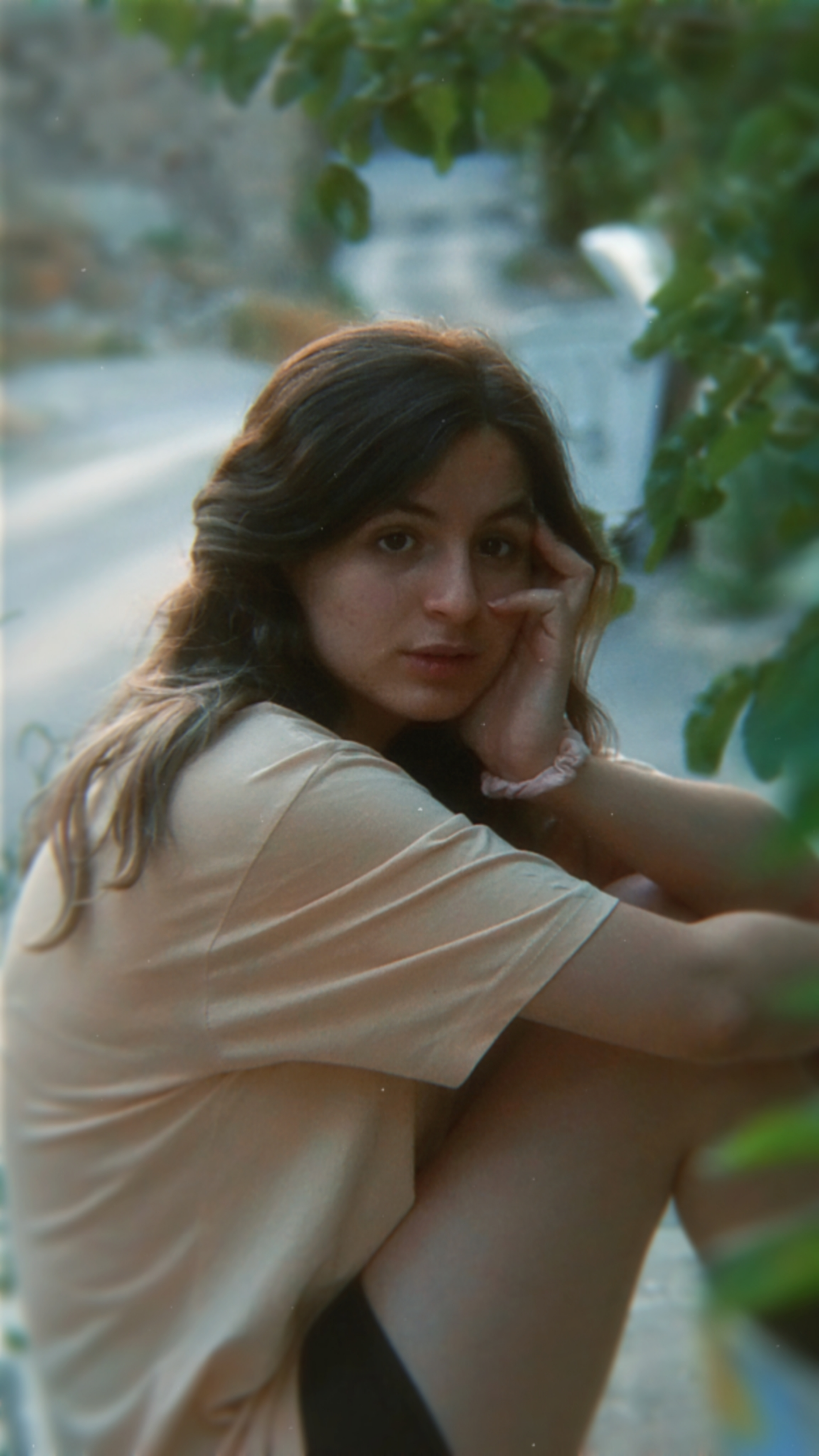 A young woman in a casual t-shirt and shorts sitting thoughtfully outdoors.