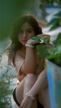 A young woman enjoying a peaceful moment surrounded by green leaves in a park setting.