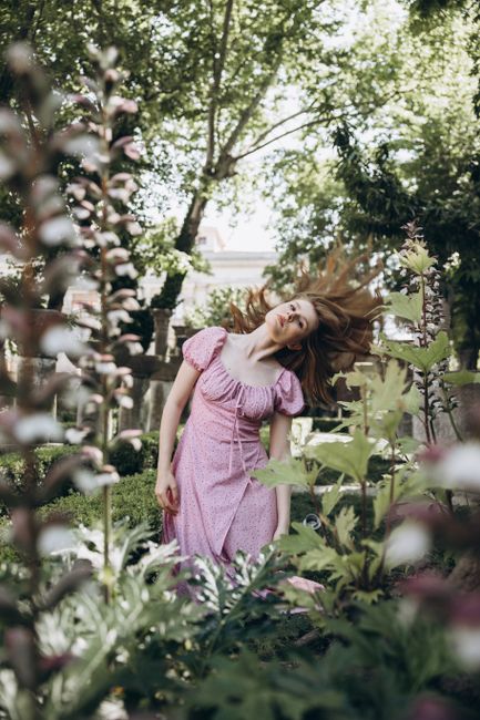 Young woman in pink dress amidst blooming garden, embracing summer's vitality.
