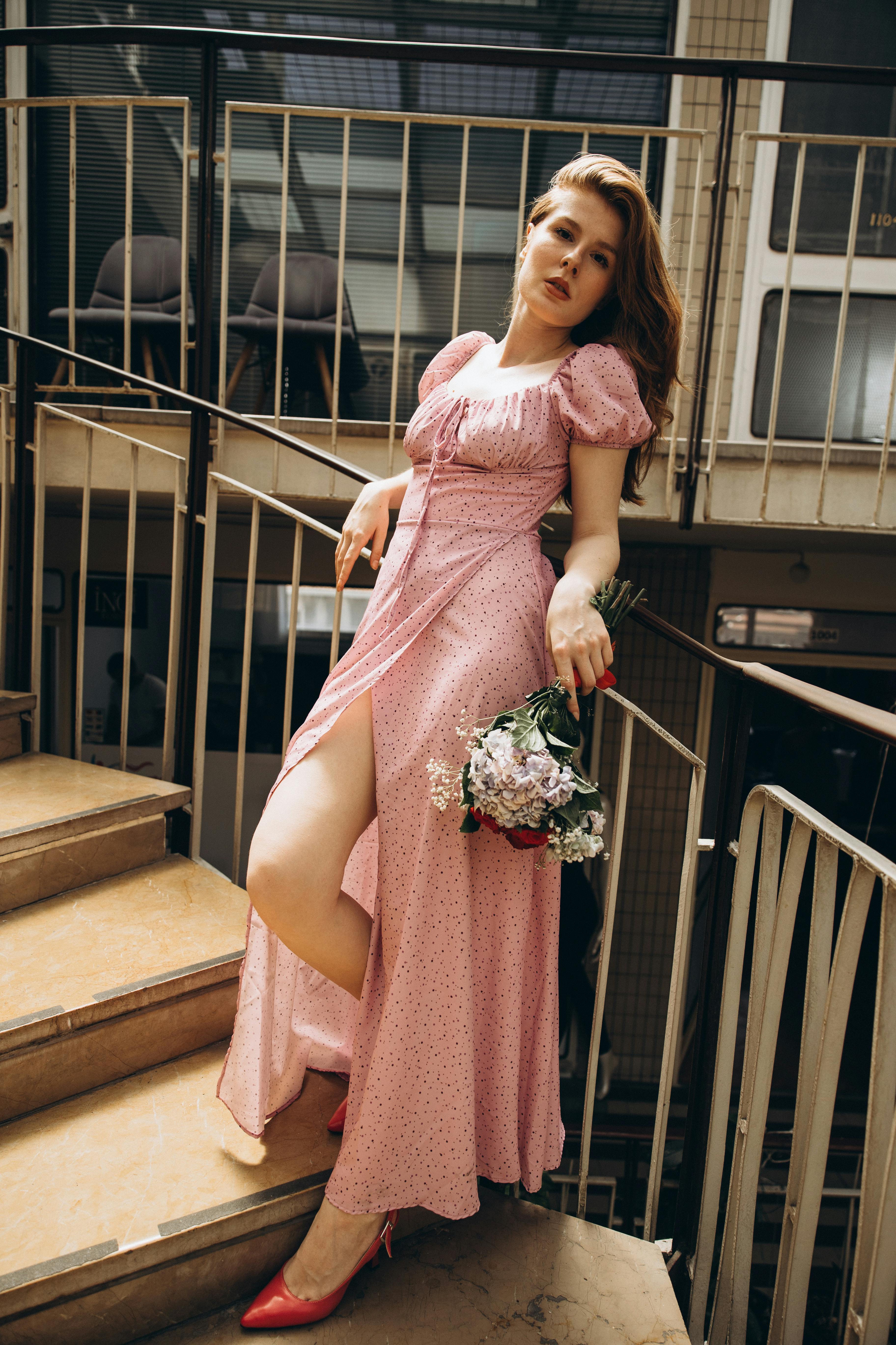 a woman in a pink dress is posing on some stairs