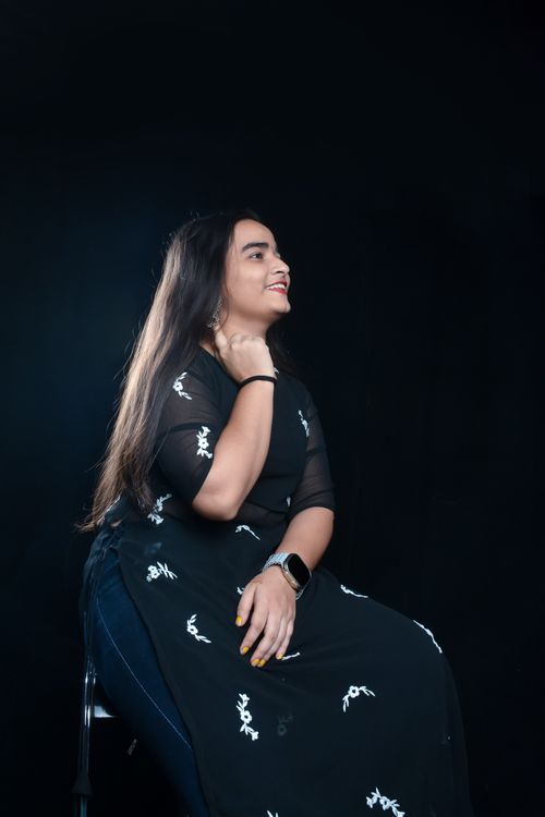 Free Portrait of a young woman sitting and smiling in a studio with a dark backdrop, showcasing elegance and natural beauty. Stock Photo
