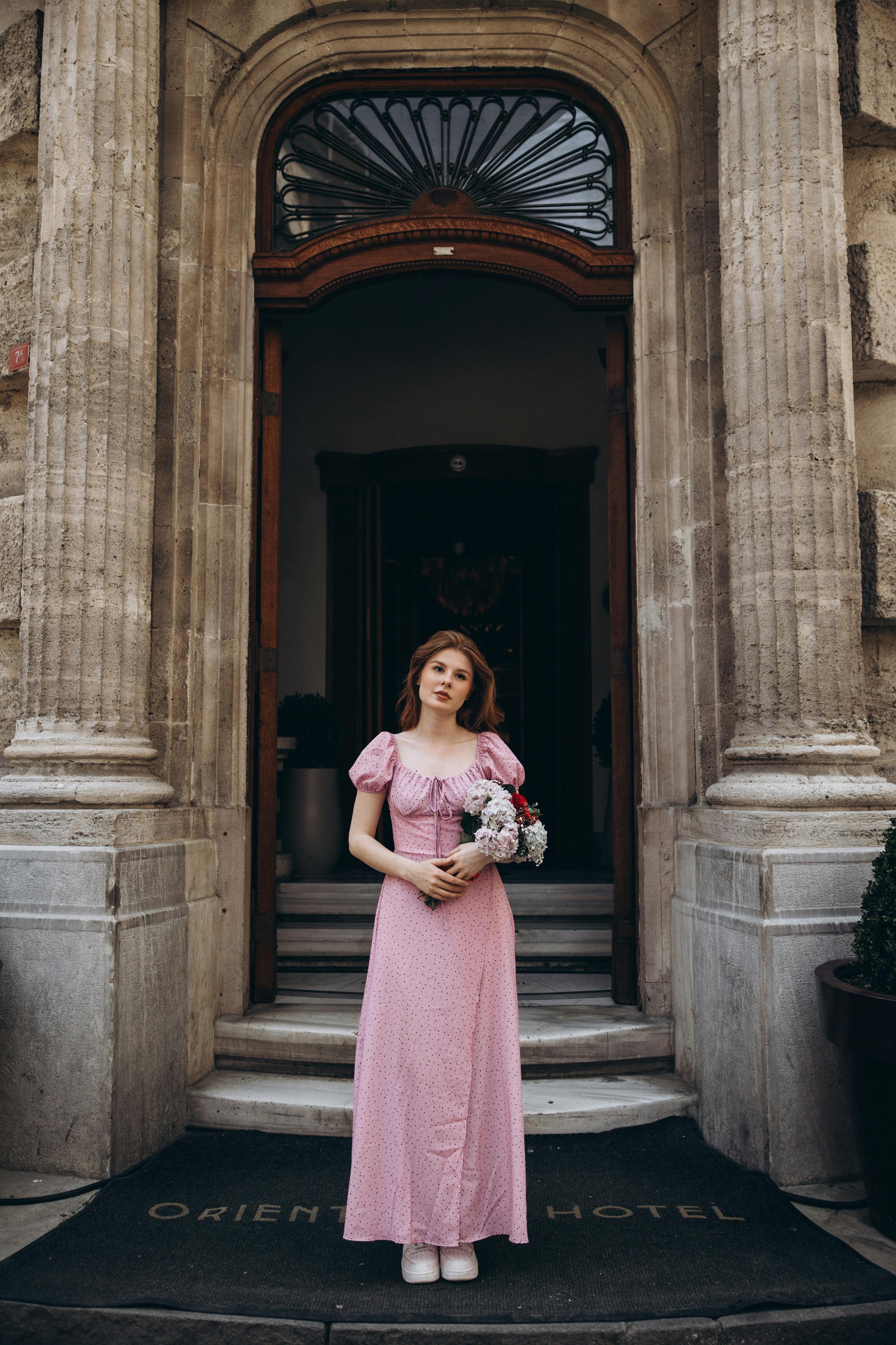 a woman in a pink dress stands outside a building