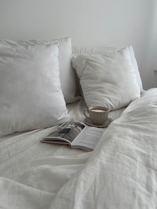 Free A tranquil bedroom setting with white linens, pillows, a cup of coffee, and an open book on bed. Stock Photo