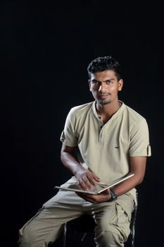 Portrait of a man sitting and reading a book on a chair against a black background.