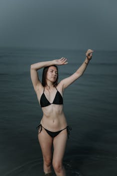 Young woman stands in the ocean, exuding serenity with arms gracefully raised.