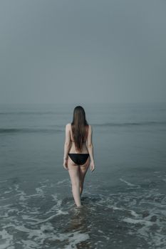 A woman with long hair walks into the sea, embracing tranquility on a summer day.