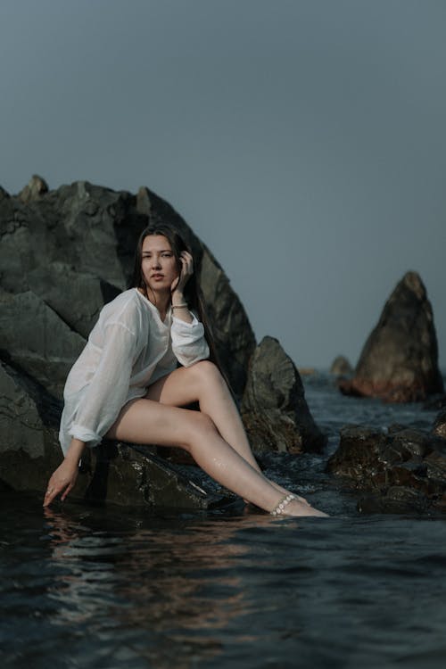 Young Woman Sitting on a Rock on a Shore 