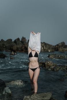 A woman wearing a bikini standing in the ocean by rocks on a vacation.