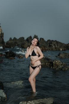 A woman in a bikini posing gracefully on a rocky shore, showcasing elegance and confidence.