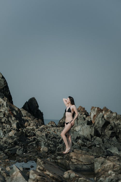 Woman in a Bikini Standing on a Rocky Shore 