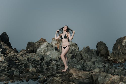 Young Woman in a Bikini Standing on a Rocky Shore 