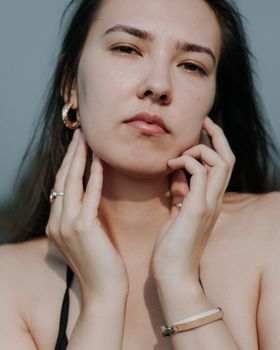 Close-up portrait of a woman with jewelry, serene expression outdoors.