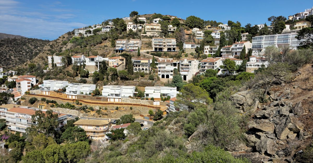 Scenic view of hillside residences with a backdrop of green hills, under a clear blue sky.