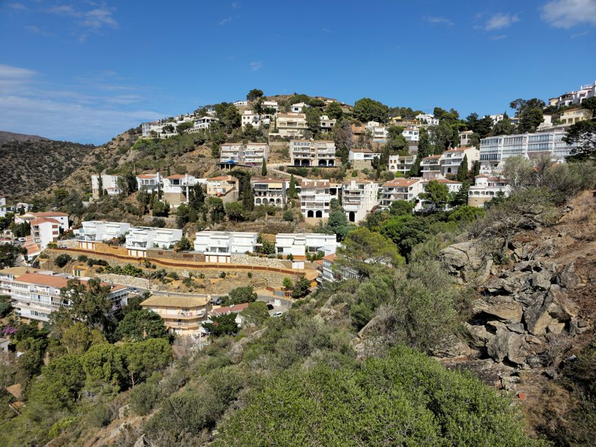 Vista escénica de residencias en la ladera con un fondo de colinas verdes, bajo un cielo azul claro.