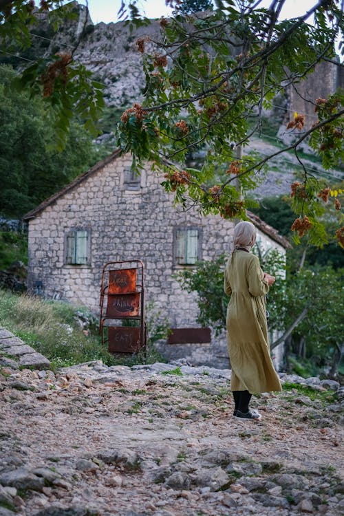 A Woman in a Dress Standing near an Old House 