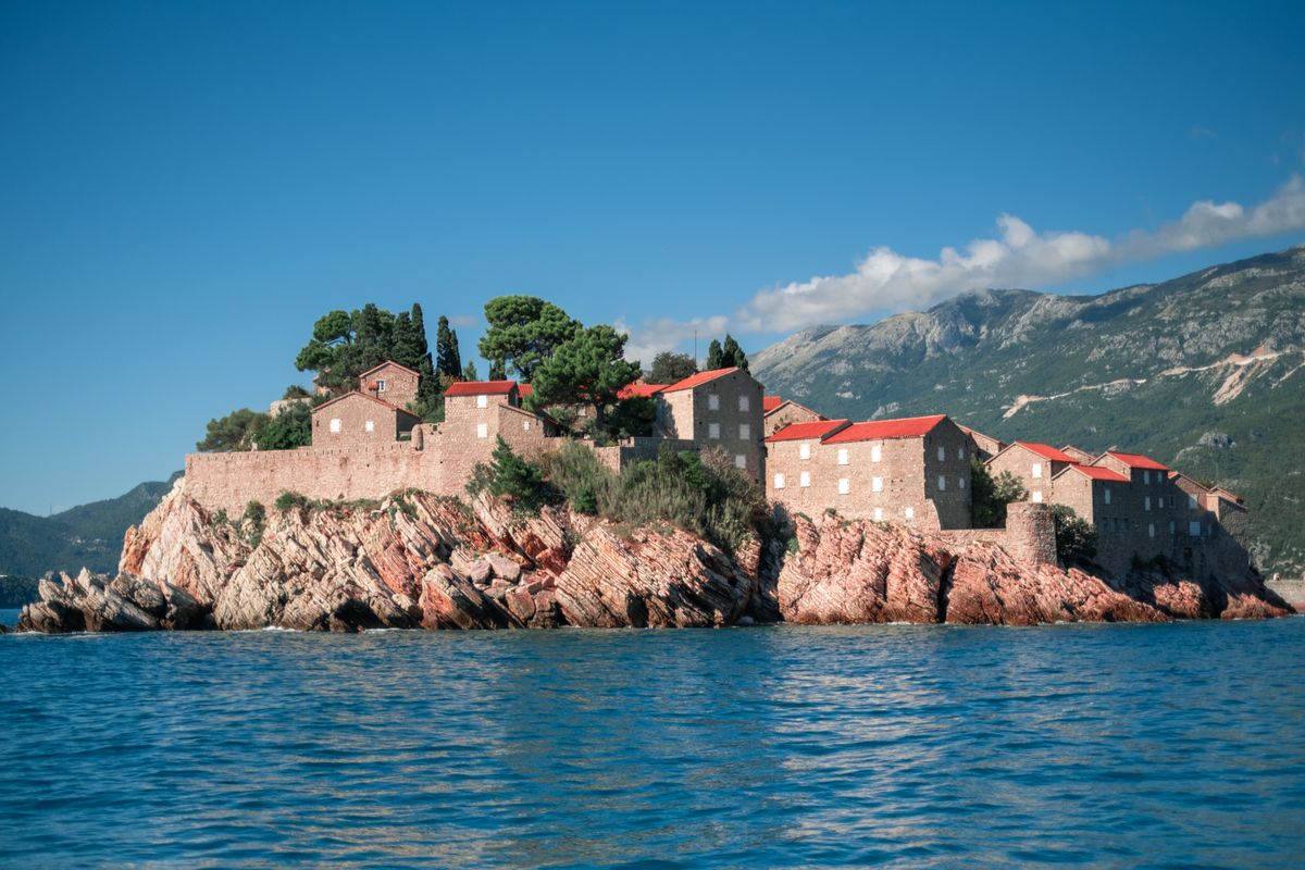Insula-fortăreață Sveti Stefan, cu căsuțe de piatră cu acoperiș roșu, încadrată de munți