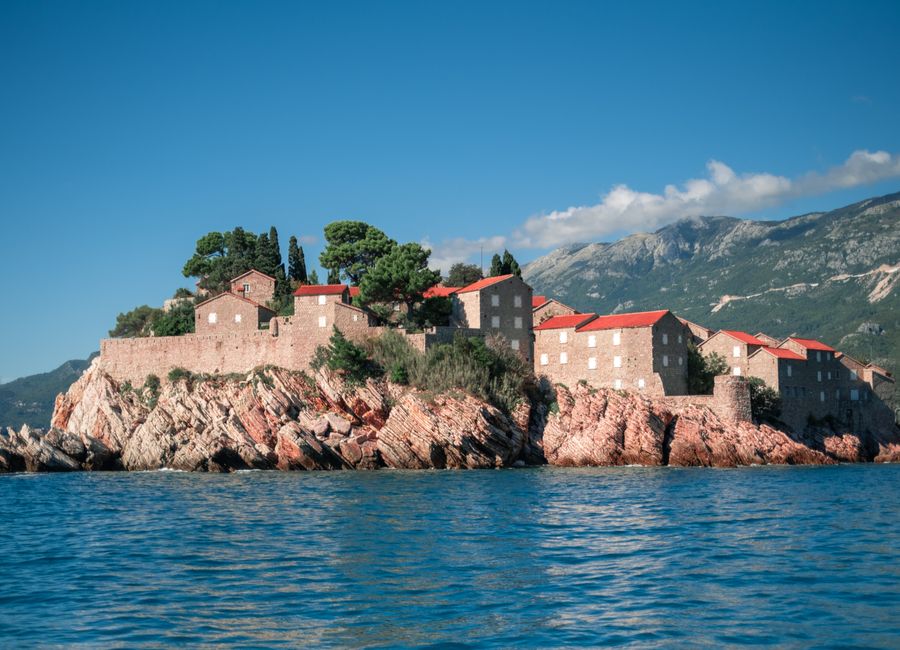 Sveti Stefan, Montenegro, stunning island fortress with red-roofed buildings on the Adriatic Sea, framed by mountains.