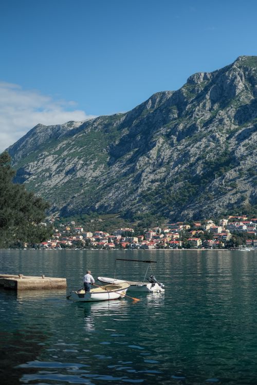 Free A picturesque lake with a small boat and a distant mountainside village under a clear blue sky. Stock Photo