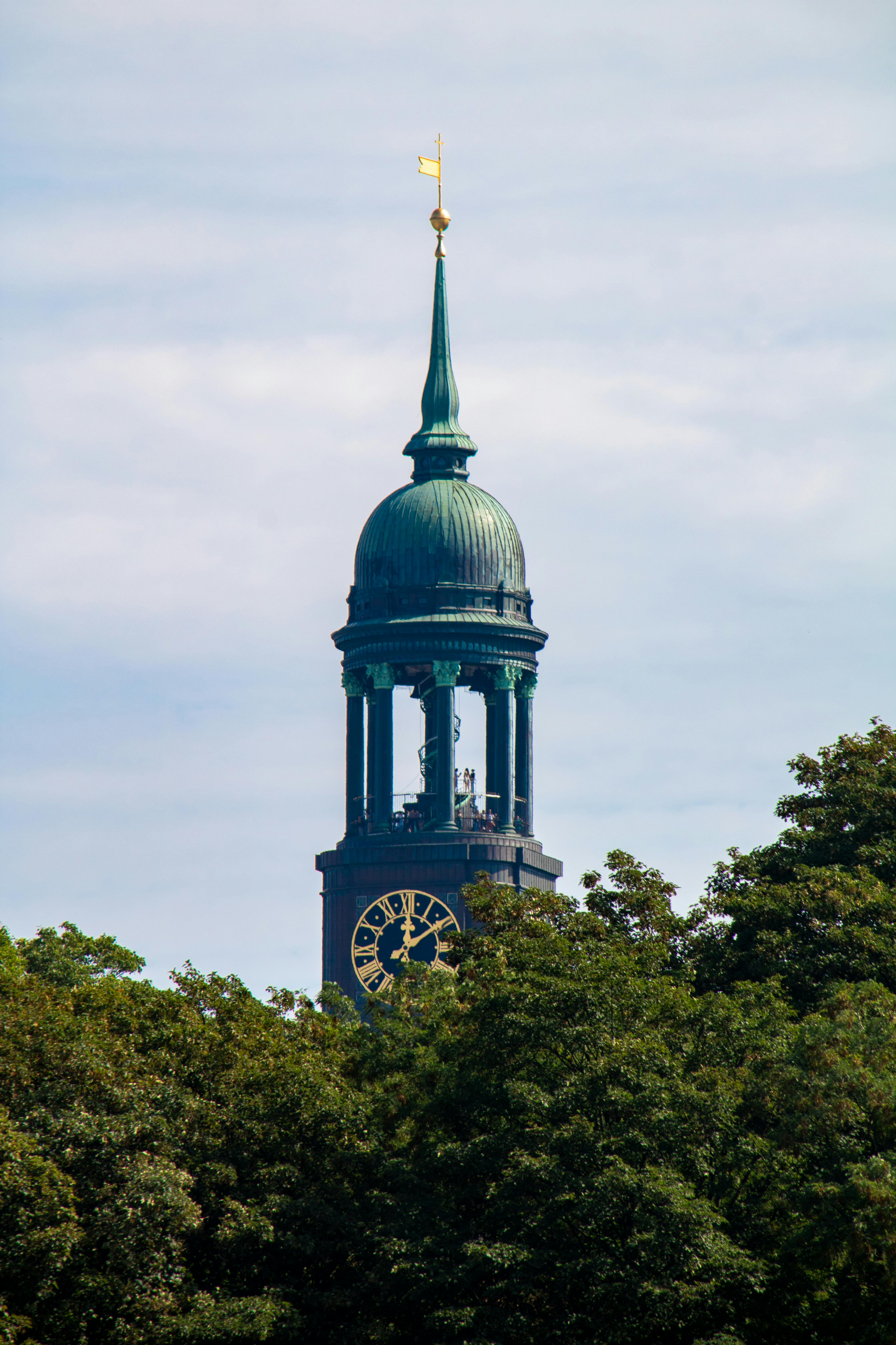 Baroque architecture of St. Michael's Church tower in Hamburg, Germany, surrounded by lush greenery on a bright day.