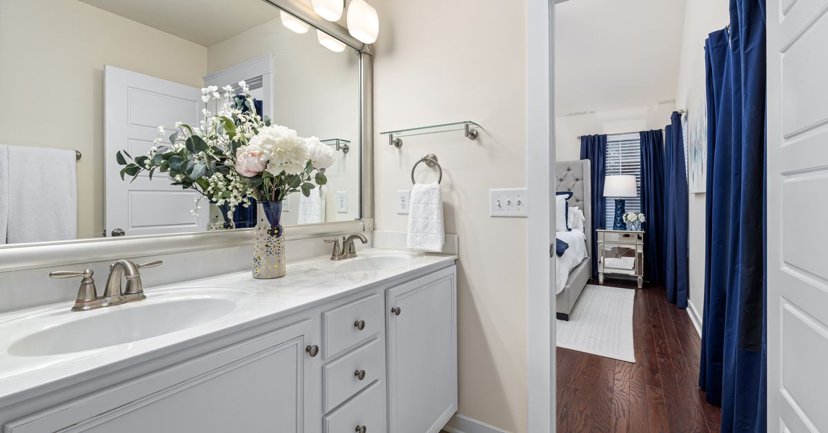 A contemporary en suite bathroom leading to a stylish bedroom with white and blue decor.