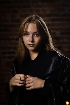 Portrait of a woman in a black leather jacket against a brick wall background.