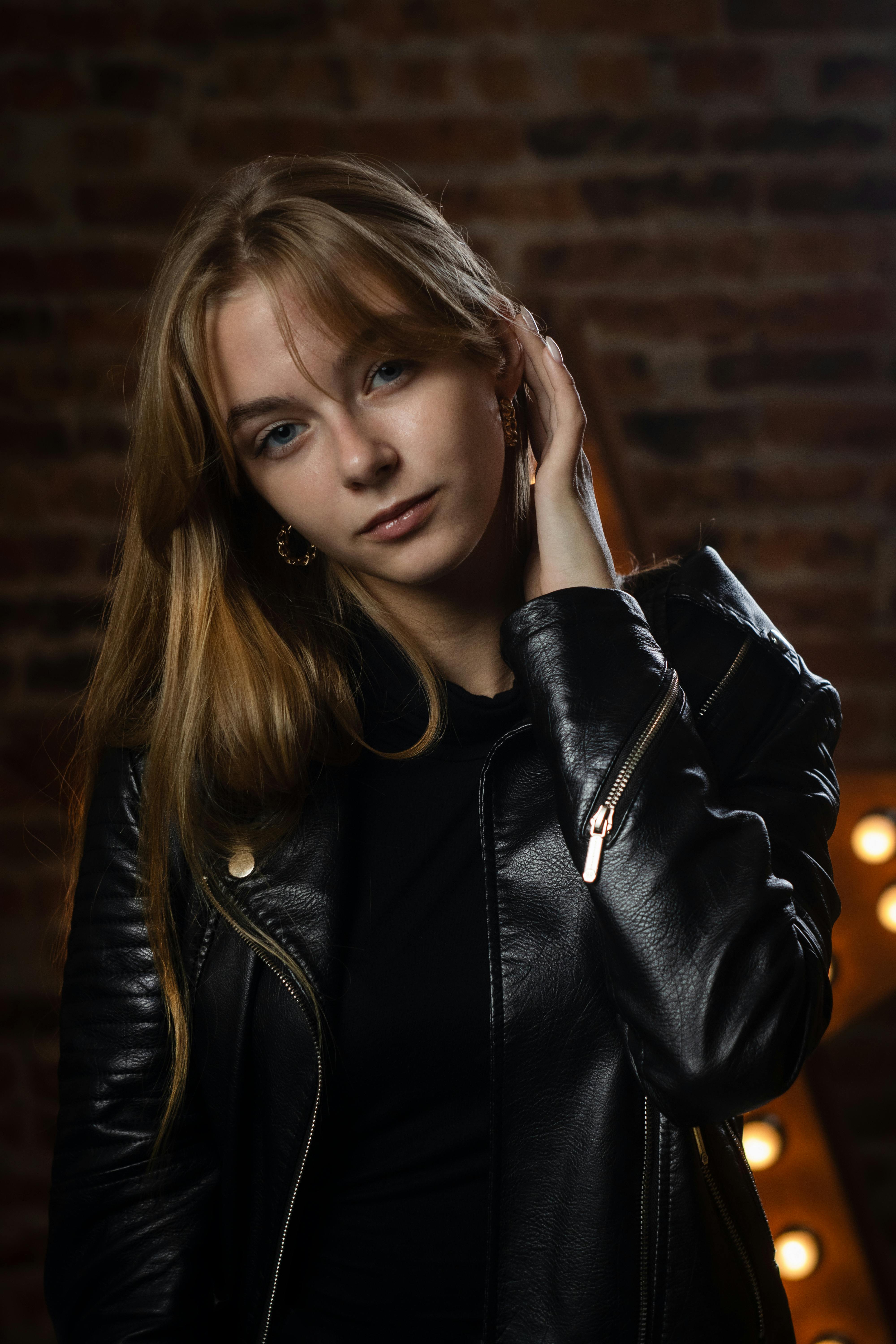 Stylish portrait of a woman in a black leather jacket indoors at night.