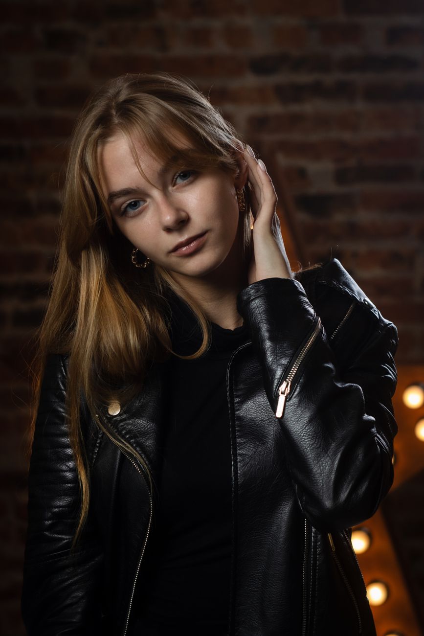 Stylish portrait of a woman in a black leather jacket indoors at night.
