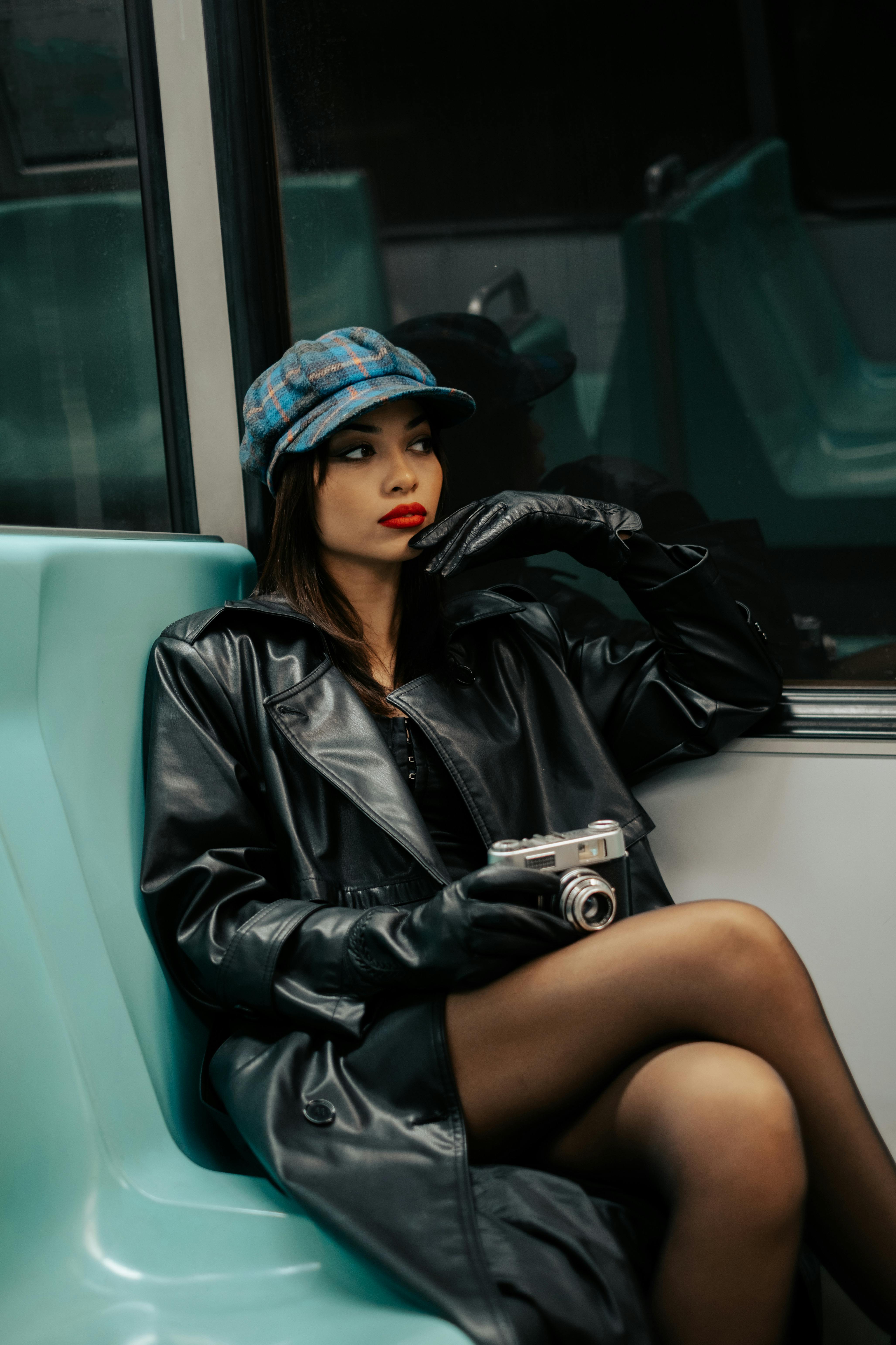 Elegant woman in leather coat and hat holding camera on subway. Modern fashion vibe.