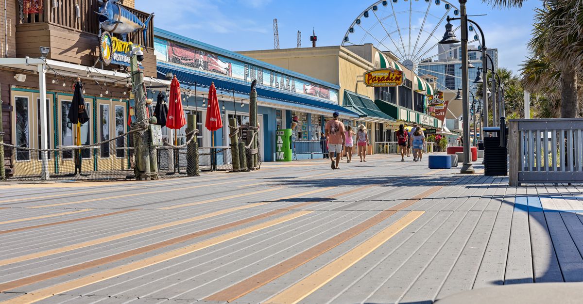 Explore the lively Myrtle Beach boardwalk with shops, a Ferris wheel, and visitors in the summer sunshine.