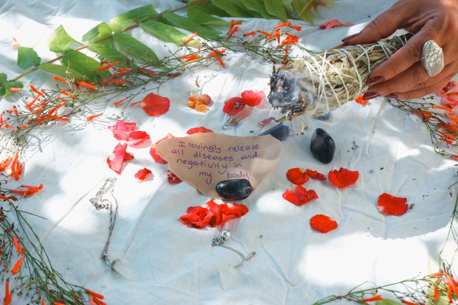 A tranquil ritual setup with sage bundle and petals on white fabric in sunlight.