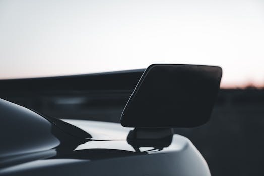 Close-up of a sleek sports car spoiler silhouette against a twilight sky.