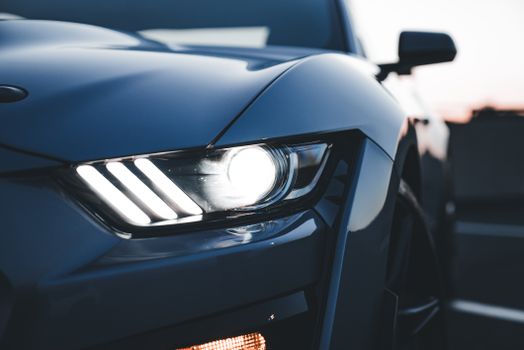 Dramatic close-up of a car's headlight during sunset, highlighting its sleek design.