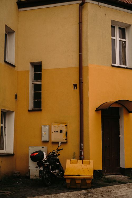 Free A quiet urban alley featuring a yellow building facade and parked scooter. Stock Photo