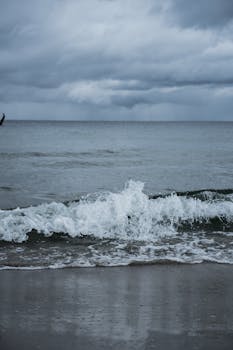 A moody scene of ocean waves crashing on a beach under cloudy skies, perfect for dramatic coastal themes.