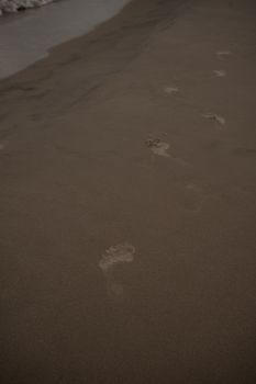 Footprints leading along a wet sandy beach with waves approaching at dusk.