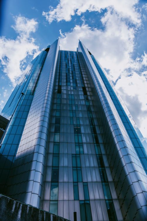 Free Low angle shot of a modern skyscraper with reflective glass facade under a blue sky filled with clouds. Stock Photo