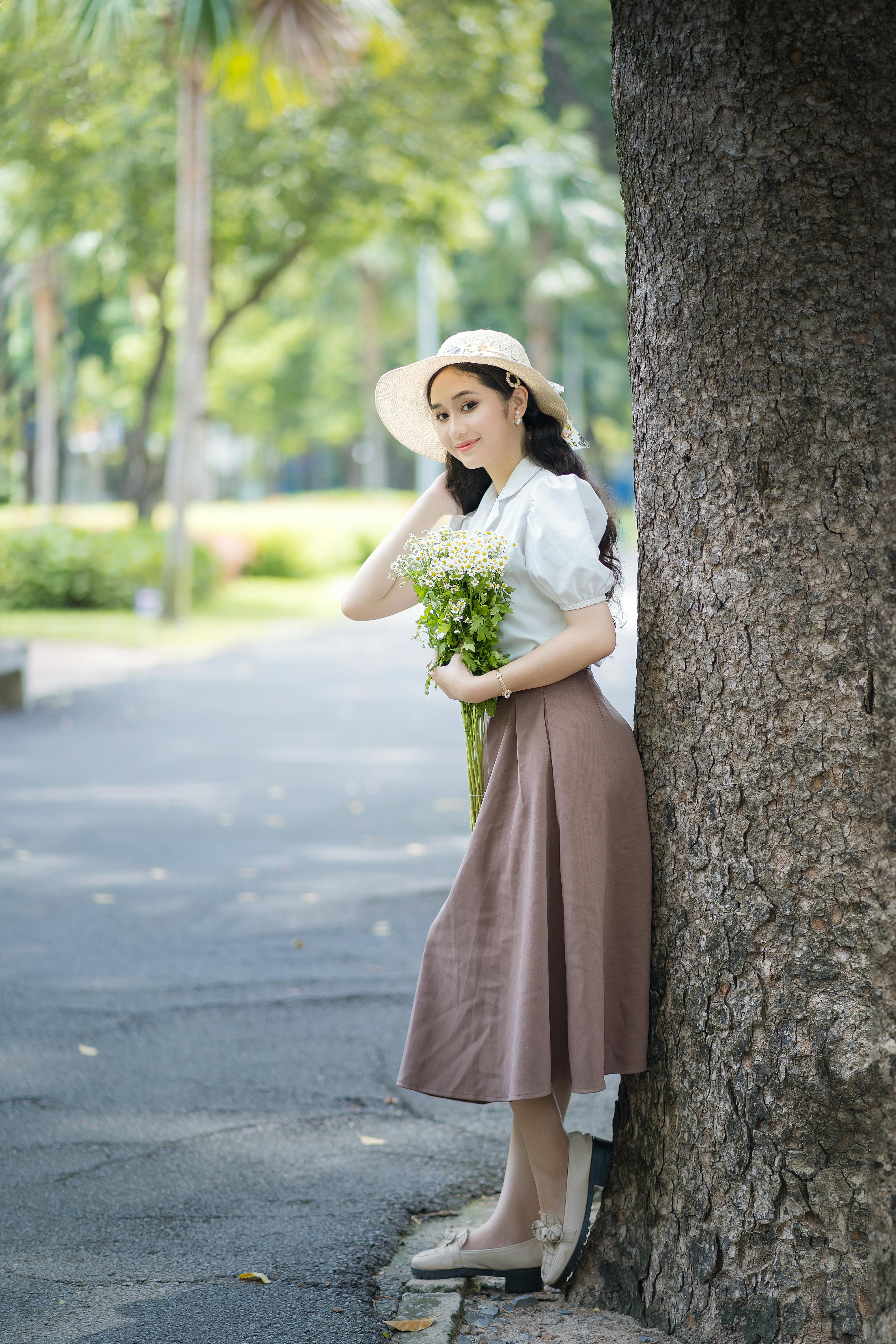 Young woman in stylish attire holding a bouquet in a summer park.