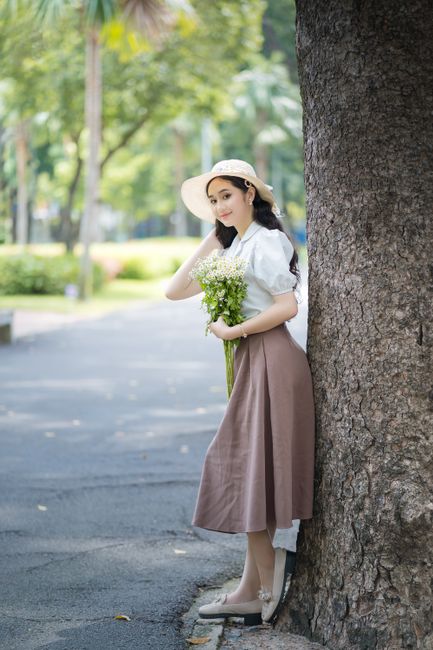 Young woman in stylish attire holding a bouquet in a summer park.