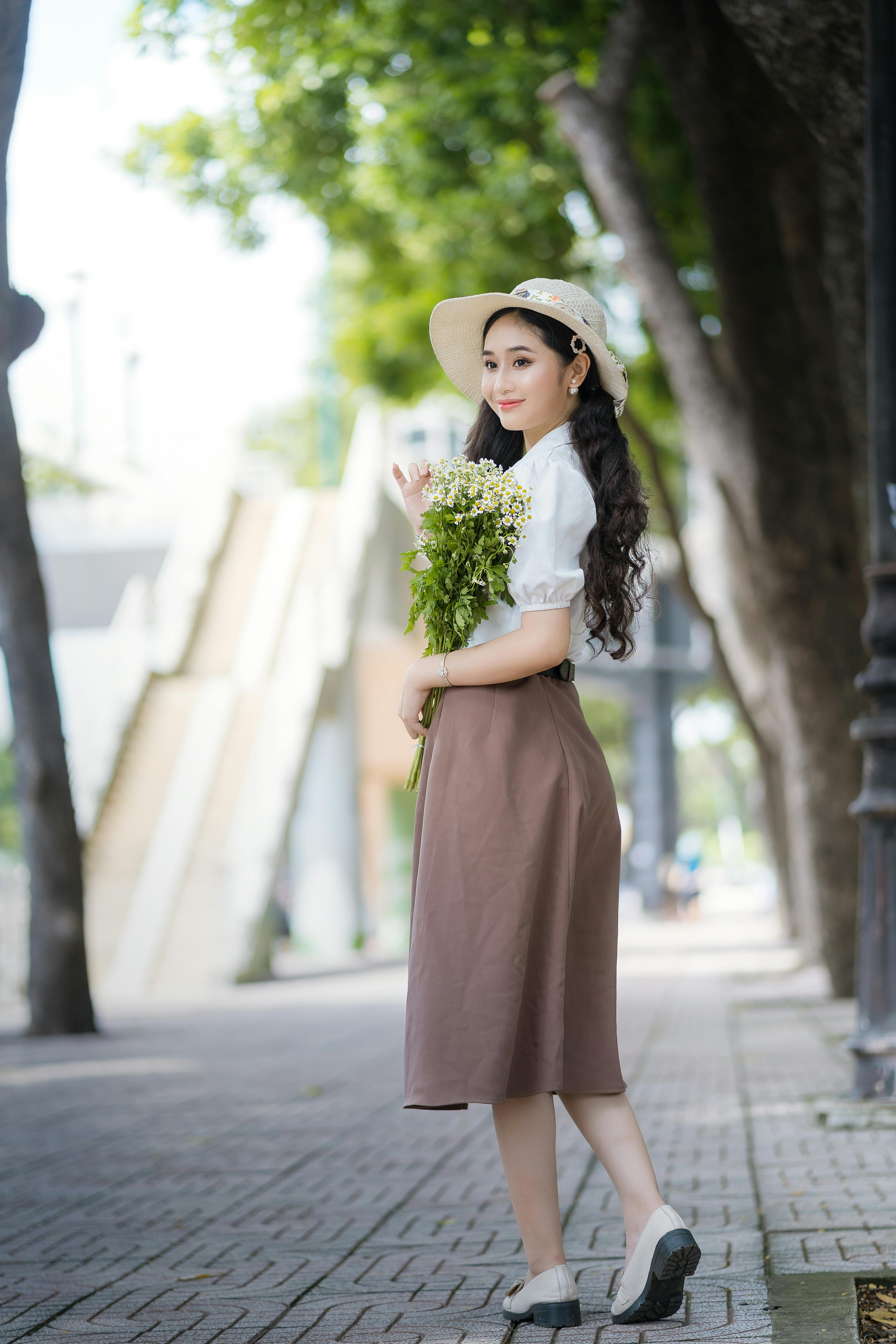Charming young woman holding flowers on a vibrant city street, exuding happiness and style.