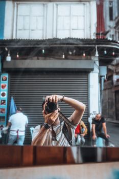 Photographer captures city reflection in mirror on urban street.