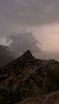 A rocky mountain peak under moody, cloudy skies during dusk, creating a dramatic scene.