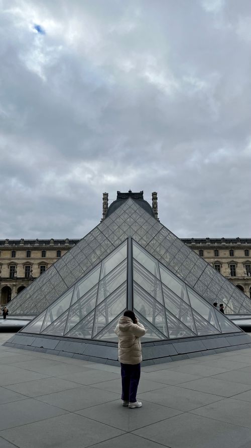Free Person standing in front of the iconic Louvre Pyramid on a cloudy day. Stock Photo