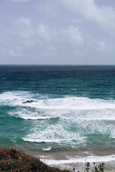 A breathtaking view of waves crashing on the rugged coastline under a cloudy sky.