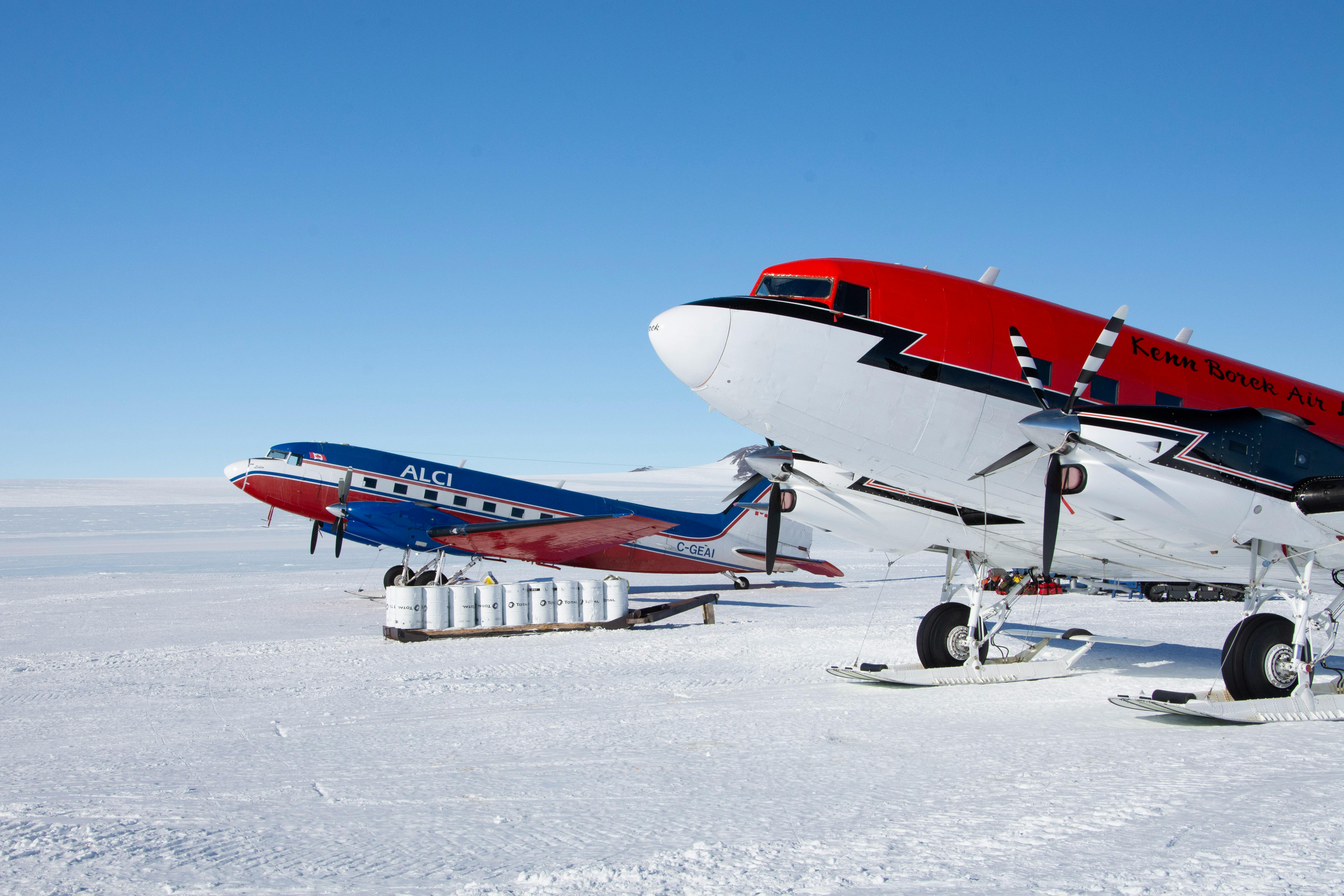 Two vibrant aircraft parked on a snowy Antarctic runway under a clear blue sky.