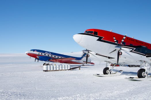 Two vibrant aircraft parked on a snowy Antarctic runway under a clear blue sky.